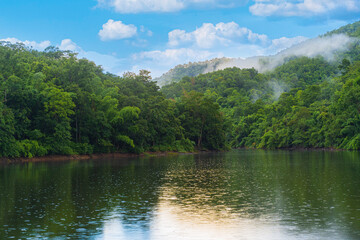 A small lake in Thailand surrounded by mountains with lush green forest and mist.