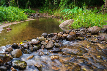 A small waterfall with many rocks in the stream surrounded by trees in the mountain forest.