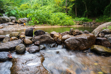 A small waterfall with many rocks in the stream. Surrounded by trees in the mountain forest.