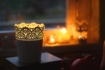 Vintage books, reading glasses, cup of tea or coffee, bowl of cookies, pumpkin and lit candles on the table. Hygge at home, fall atmosphere. Selective focus.