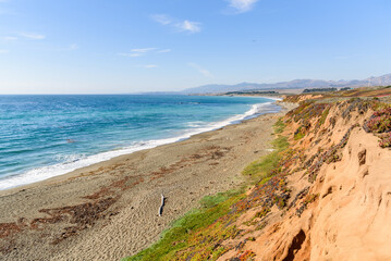 Fototapeta na wymiar Empty sandy beach at the foot of a steep cliff along the coast of central California on a sunny autumn day