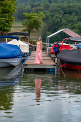 Pretty young girl at marina standing on the dock in pink dress