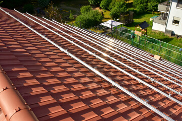 Dachdecker beim Aufbau einer Photovoltaikanlage auf einem neu gedeckten Ziegeldach: Schienensystem ist montiert und die Anschlüsse sind gelegt