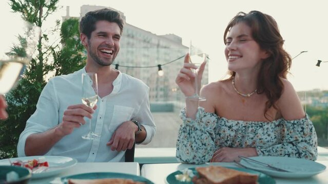 Smiling couple clinking glasses while celebrating with friends on restaurant balcony