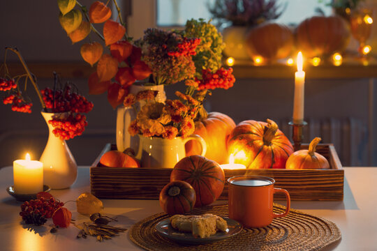 orange cup of tea and autumn decor with pumpkins, flowers and burning candles on table