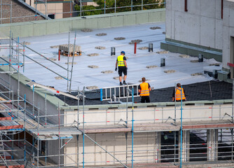 Birdseye view of roofer waterproofing the flat roof of a commercial building. - obrazy, fototapety, plakaty