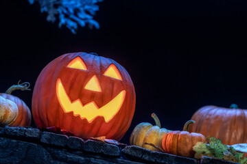 A smiling Jack O Lantern sitting on an old wooden porch with small pumpkins and fallen leaves as a Halloween. © CMANNPHOTO