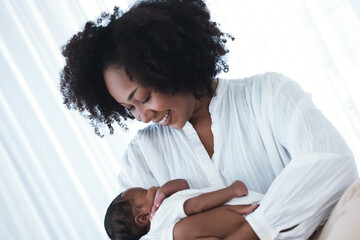 Happy African American Mother holding her newborn infant baby while sitting on bed in hospital....