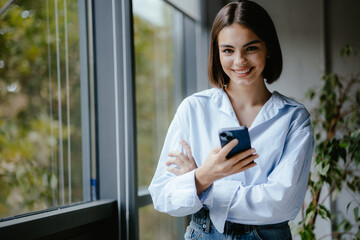 Smiling woman with her phone in an office. Corporate person smiling in with a telephone in hands.