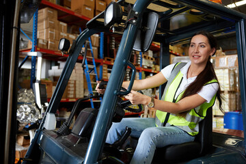 Fototapeta na wymiar female worker driving a forklift and looking to something in warehouse storage