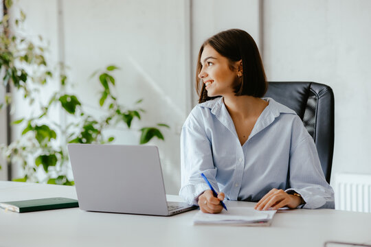 Woman with papers in an office working at her desk with a laptop in front of her.
