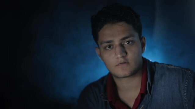 Close-up shot of a man in a denim shirt sitting and smiling in front of the camera, cinema-like light.HD stock footage.High production quality.Night-time shot of a man sitting and waiting for someone.