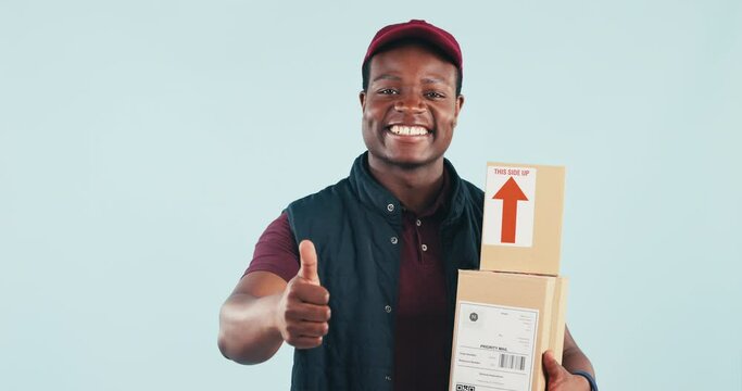 Delivery man, boxes and thumbs up in studio with face, portrait and smile for supply chain by blue background. African courier, cardboard package and icon for ecommerce, logistics or emoji for review