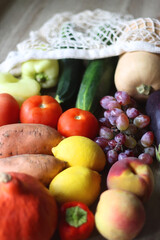 Reusable mesh bag with seasonal fruit and vegetable on wooden background. Late summer or early autumn. Selective focus.