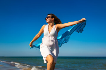Happy beautiful woman holding shawl walking on sunny beach
