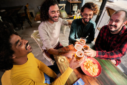 Four happy male friends toasting with beers at a bar, having fun and enjoying the evening together. Top view image with copy space.