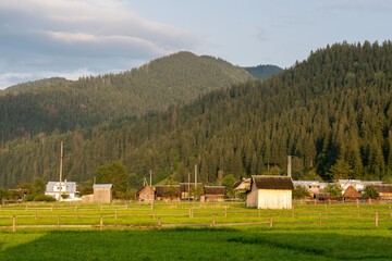 The Carpathian Mountains after the rain, sunny day at the beginning of the autumn. Rural wooden and brick village houses on a meadow in the mountains.