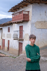 Boy dressed in a green sweatshirt and Turkish-style babouche pants with an old house behind him