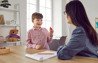 Female speech therapist with a little boy patient practicing private development lessons. Young woman teacher with a child training articulation and pronunciation. Speech practice and therapy concept - obrazy, fototapety, plakaty