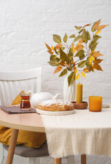 Autumn home decoration. Apple pie, Vase with autumn leaves branches, White teapot, candles on round wooden table on white background.