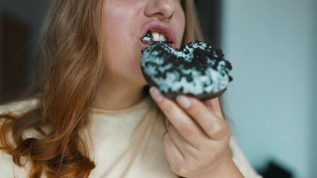 Close up portrait of a hungry 30s woman eating donuts with white frosting. Eating donut when takeout and delivery. Fast food takeaway back home. High quality FullHD footage. High quality FullHD