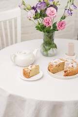 Summer home decoration. Apple pie, Vase with summer flowers, white teapot, candle on round white table on white bricks background.