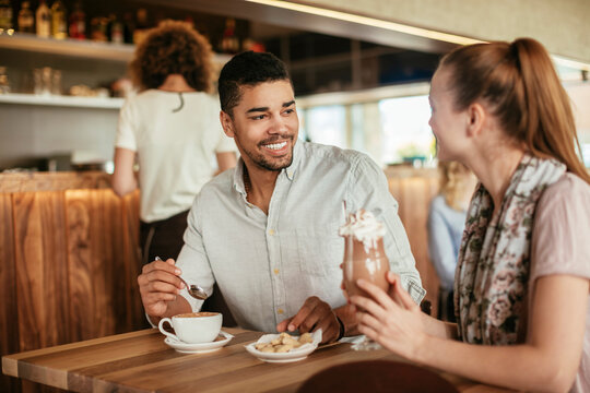 Young interracial couple having coffee together while on a date in a cafe or bar - Powered by Adobe