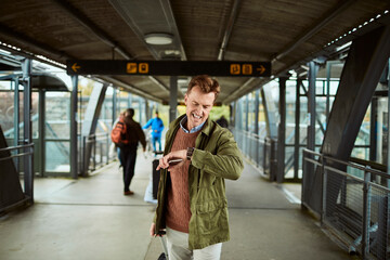 Middle aged man looking at his watch and expecting the arrival of his train at the train station