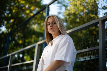 Young blonde woman in a white shirt looks at the camera on the street, bottom view