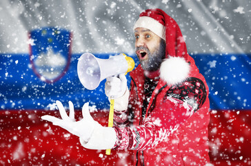 Santa Claus shouts into a megaphone and shows a hand gesture against the background of the flag of Slovenia