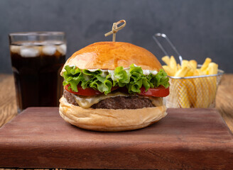 Cheeseburger with lettuce, tomato and mayonnaise over wooden board with french fries and soda