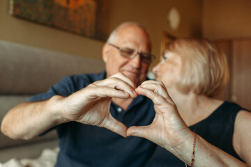 An elderly couple shows a heart with their hands as a sign of love, look at each other.