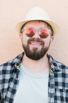 Close-up portrait millennial man wearing summer hat and sunglasses and plaid shirt smiling happy near wall - travel vacations and summer holiday concept