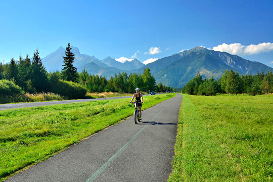 Happy  woman dressed in cycling clothes and helmet, riding a bicycle on the asphalt out-of-town bicycle path.
Active sporty people concept image.
High Tatras mountains at background.