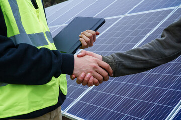 Close-up view of two individuals shaking hands in front of solar panels.