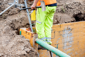 Groundworker builder using steps ladder to get out of the deep drainage eaxcavation trench support box. Builder going up using ladder. Safe workplace fall prevention concept - obrazy, fototapety, plakaty