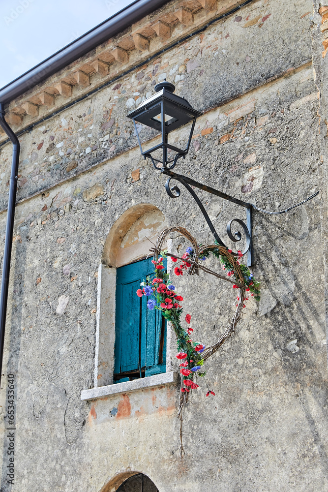 Poster Rustic house wall in Tuscany, with a street lantern and a heart wreath of flowers.