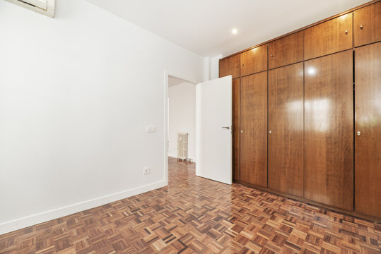 An empty room with a large built-in wardrobe with wooden doors covering one wall
