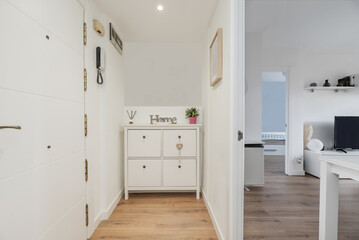 Hallway of a home with a white drawer unit, access door from the street and access to another room with white furniture