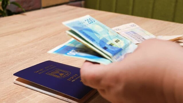 Israeli passport and Ukrainian passport in hands. Shekels and hryvnias, the national currency. Concept: repatriation, change of citizenship, aliyah, absorption basket.