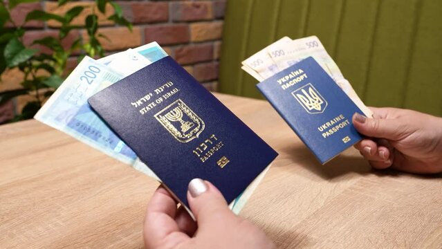 Israeli passport and Ukrainian passport in hands. Shekels and hryvnias, the national currency. Concept: repatriation, change of citizenship, aliyah, absorption basket.