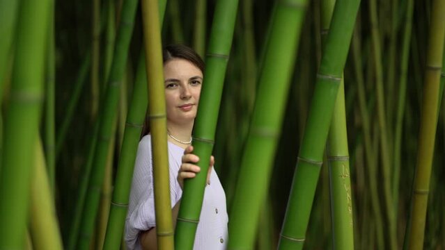 a girl tourist in a dress stands in a bamboo grove and looks at the camera through the bamboo.