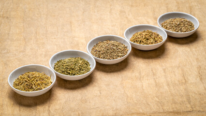 herb spices - dried leaves of parsley, rosemary, thyme, basil and oregano, collection of small ceramic bowls on a textured bark paper