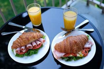 six pieces of bacon rolled into a sandwich croissant Lettuce leaves Brie cheese breakfast chic food on a black plate restaurant serving serving tomato outdoors. summer