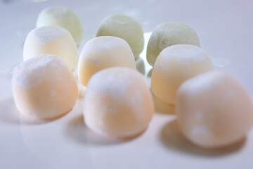 different flavors of Asian dessert mochi, a hand takes out sweet ice cream made from peas and rice starch dough from a box. white plate