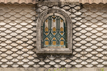 Old house wall with a badass concrete fish-scale design. Vintage window. Wall covered in lush moss. Harsh lighting, vibrant contrasting shadows