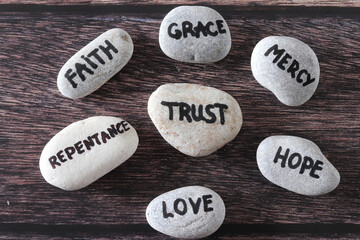 Trust, mercy, faith, grace, love, repentance, and hope handwritten words on stones. Top view....