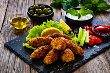 Kibbeh - Arabic style seared meatballs mixed with bulgur groats and mint yogurt on wooden table 