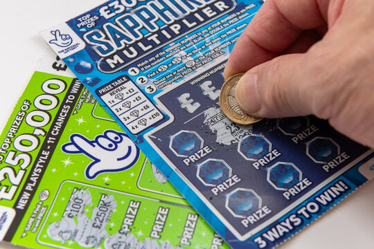 London. UK- 09.27.2023. Two National Lottery scratch cards isolated in white with a player scratching a card with a coin.