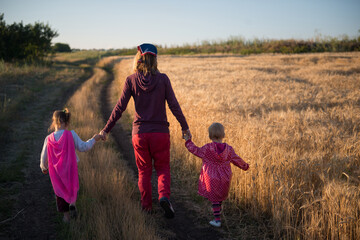 Mother and two children walk along a scenic road through wheat field. Happy family. - 653453249